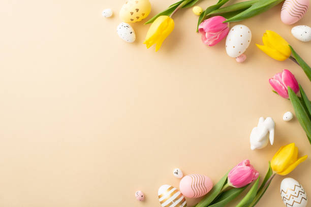 istock Easter decorations concept. Top view photo of colorful easter eggs ceramic easter bunny and tulips on isolated light beige background with empty space 1469675201