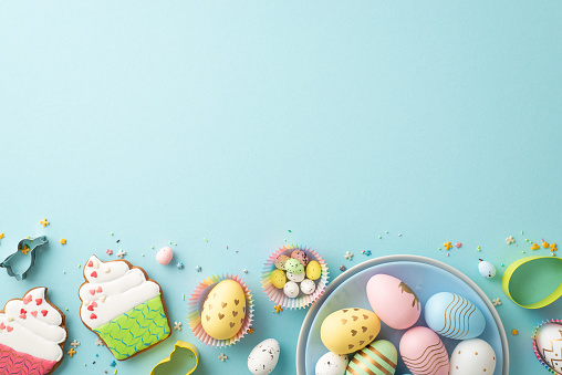 Easter cuisine concept. Top view photo of colorful easter eggs in plate paper baking molds cupcake shaped gingerbread and sprinkles on isolated pastel blue background with empty space