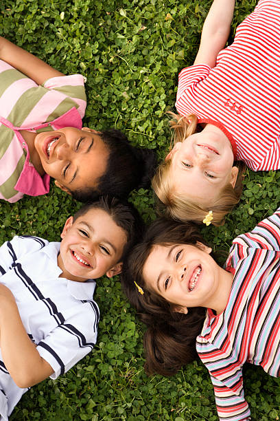 Four happy kids laying with heads together outside in clover stock photo