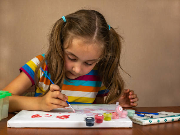 istock A little girl enthusiastically paints with paints on a white canvas. 1469676476