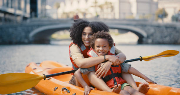 ritratto di madre, bambino e kayak sul fiume o sul lago, divertimento tempo di vacanza con sport acquatici, estate e felice avventura in svezia. viaggio, vacanza e donna nera con figlio, sorriso e canoa nel canale della città - skiff time travel locations sports and fitness foto e immagini stock