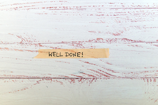 motivational message 'well done' handwritten on colorful washi tape against white wooden background