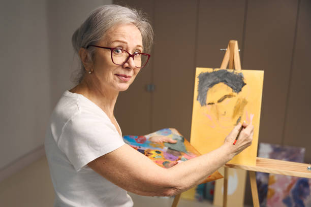 istock Talented elderly woman stands at an easel with a palette 1469684509