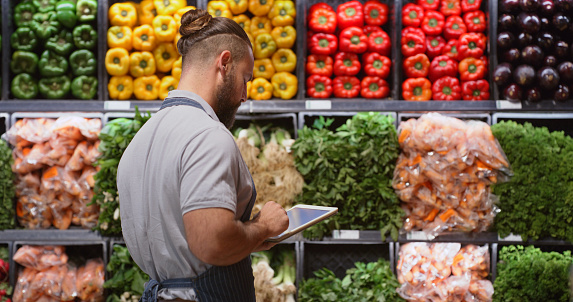 Grocery, stock take and tablet with a man at work in the vegetable or fresh produce aisle of a store. Food, counting and supply with a male employee working in a supermarket for groceries