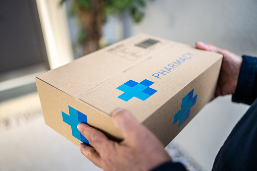 Delivery service worker hands holding cardboard box with pharmacy medications order close up