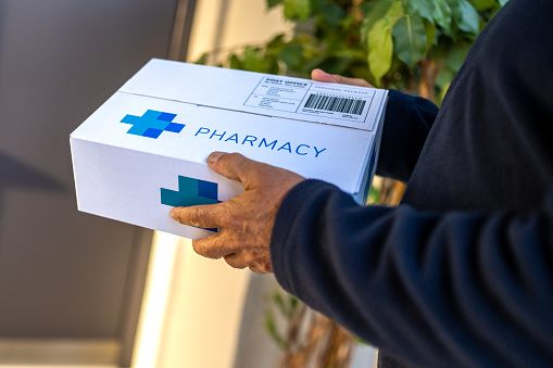 Delivery service worker hands holding cardboard box with pharmacy medications order close up