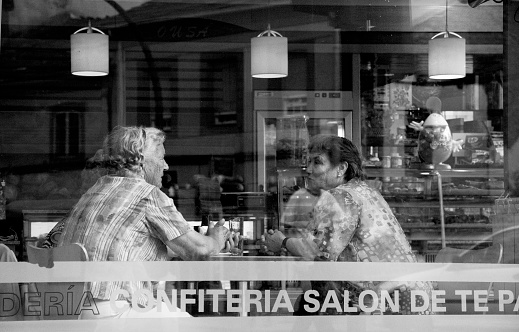 Lugo, Spain-September 10, 2010: Cafeteria window seen from the street, two senior women talking, buildings reflections. Lugo city, Galicia, Spain.