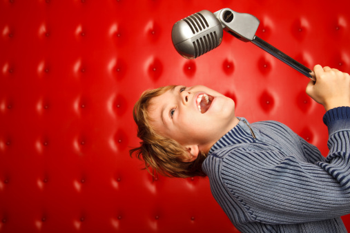 Singing boy with microphone on rack against red wall. Horizontal format