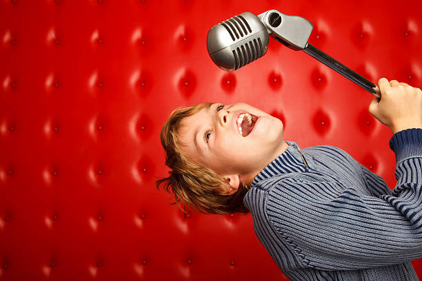 Singing boy with microphone on rack against red wall stock photo