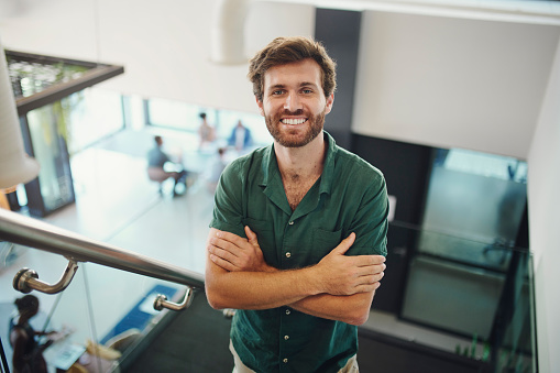 Top view, portrait and business with man, arms crossed and smile on stairs, confident entrepreneur and modern office. Startup, male leader and manager on steps, happiness and new project in workplace