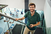 Agency, employee and portrait of man on office stairs in a company happy and smiling and holding a phone. Worker, intern or trainee excited with a positive mindset at the workplace by steps