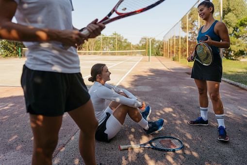 Photo of female friends relaxing in the shadows after playing a double match on a tennis court