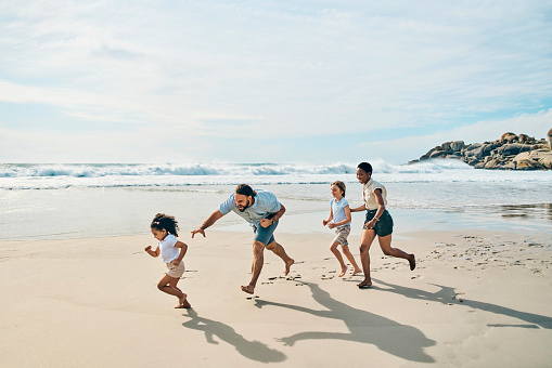 Family, bonding or beach children running in fun game, energy playing or freedom on holiday, vacation or summer travel. Smile, happy or runner kids by sea and interracial parents, man or black woman