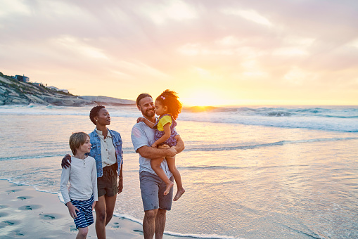 Family, walking or children carrying on sunset beach, sea or nature in relax summer holiday, bonding vacation or freedom travel. Smile, happy or ocean kids and black woman, man or interracial parents