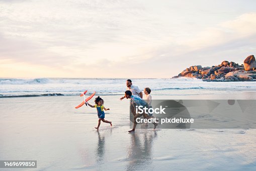 istock Happy family, running or flying toys on sunset beach or ocean in freedom holiday, energy bonding or travel playing fun. Sea, children or kids with airplane, interracial parents or aeroplane by nature 1469699850