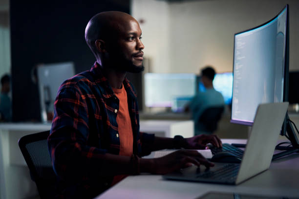 istock Computer, laptop and man in the office at night working overtime on website development project. Technology, career and professional African male webdesign developer in workplace late in the evening. 1469706261