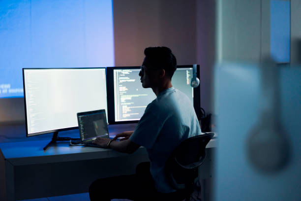 Web design, coding and Asian man with a computer for programming a website at night. Cyber security, developer and programmer reading information for a software database on a pc in a dark office stock photo