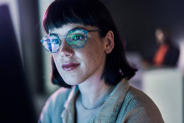 Business woman face, computer and ux coding of young employee with blue light and glasses. Digital code, hacker ai and reading of a female worker at night planning with online cybersecurity data stock photo