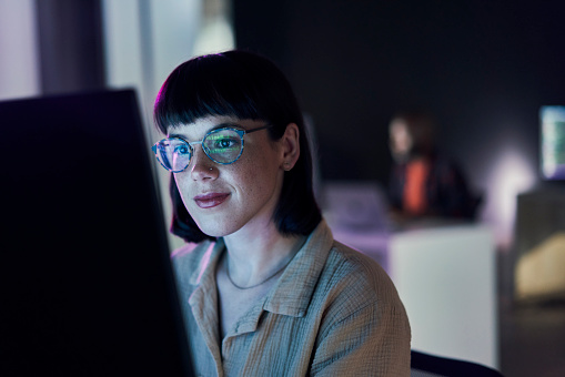 Business woman, computer seo work and coding of young employee with blue light and glasses. Digital code, female face and reading of a it employee at night planning with online ecommerce and ai data