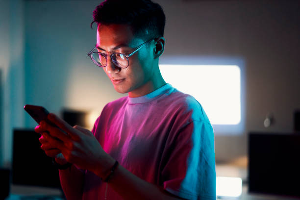 Asian man, phone or programming in night office of software development, cybersecurity review or database code safety. Programmer, developer or engineer on neon technology, web 3.0 coding or thinking stock photo