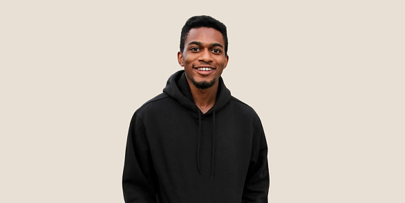 Portrait of modern smiling young african man looking at camera wearing black hoodie isolated on gray background