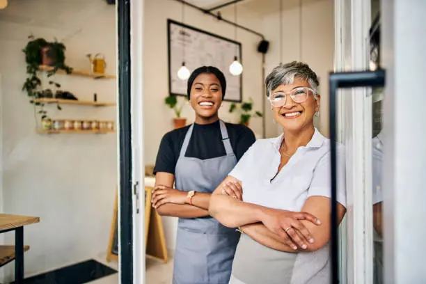 Photo of Coffee shop, senior woman manager portrait with barista feeling happy about shop success. Female server, waitress and small business owner together proud of cafe and bakery growth with a smile