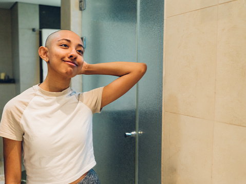 Portrait of a young woman with shaved head standing in front of the bathroom mirror