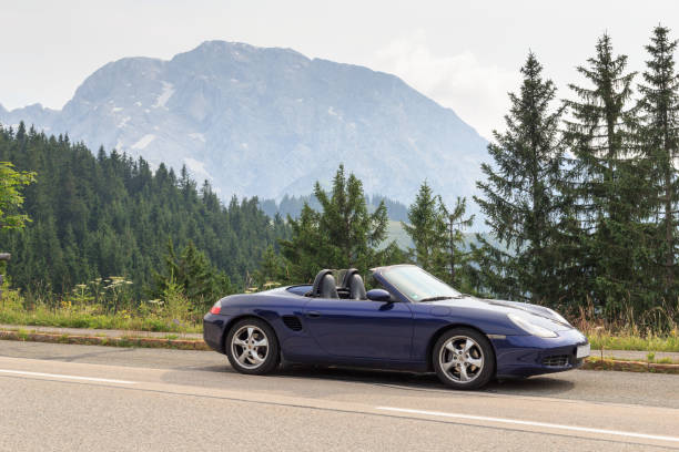 berchtesgaden, alemania - 24 de julio de 2021: roadster azul porsche boxster 986 con panorama de montaña hoher göll en rossfeldpanoramastraße (autopista panorámica de campo de caballos). es un automóvil deportivo de porsche. - germany landscape nissan roadster fotografías e imágenes de stock