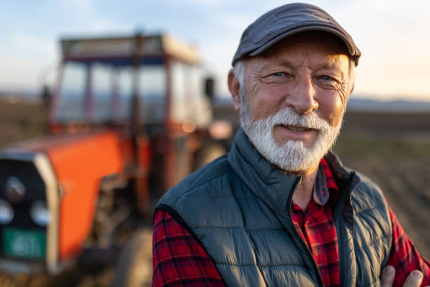 senior farmer in front of tractor in field - photography gray hair farmer professional occupation imagens e fotografias de stock