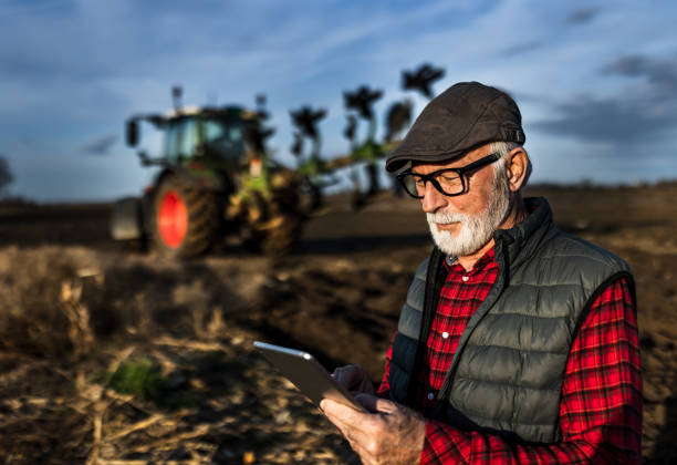 istock Senior farmer with tablet in field with tractor in background 1469735311