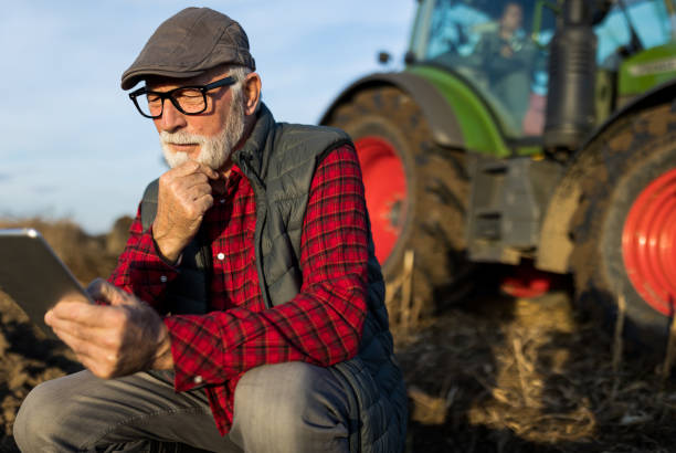 istock Senior farmer with tablet in field with tractor in background 1469735384