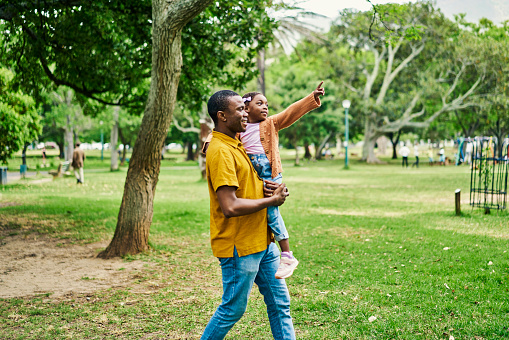 Trees, black man carrying child in park and pointing, laughing and spending happy family time together. Summer weekend, father and daughter fun in garden and happiness for girl and dad sightseeing.