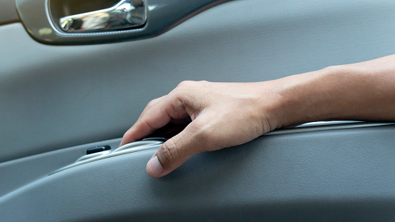 Passenger's hand holds armrests beside the door of car from the inside. Driver finger pulls the windowpane button.
