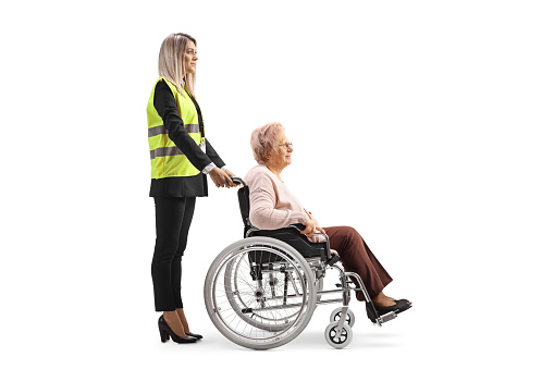 Special assitance worker standing behind a senior woman in a wheelchair isolated on white background
