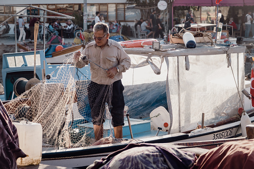 Izmir, Turkey - November 05th 2022.Fisherman straightens the nets on the fishing boat on the Izmir Foça coast