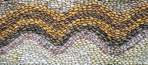 Pebbles stone wall texture background. Pebbles mosaic. Wave pattern design beach pebbles on concrete wall abstract background. Embedding individual stones in cement. Natural stone pebbles. Simple wall