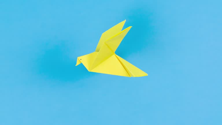 Yellow paper transforms into an origami dove that flies. Symbol of peace. Blue background.