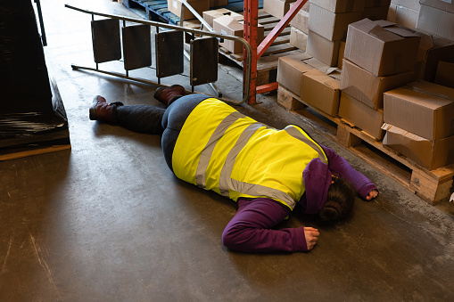 Accident in the work place, young woman lies injured after falling from step ladder onto the factory floor