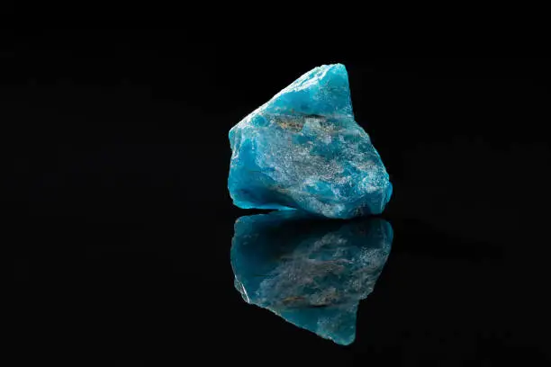 Raw Blue Apatite Mineral Stone Specimen on Reflecting Black Surface over Black Background