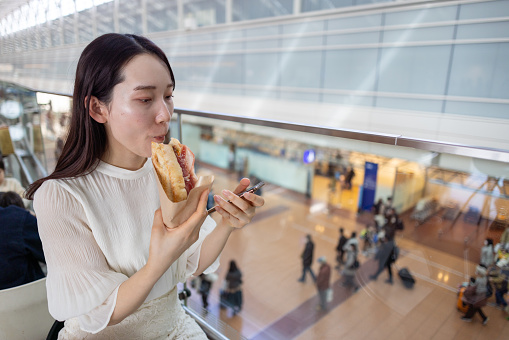 Young businesswoman eating sandwich and using smart phone in airport