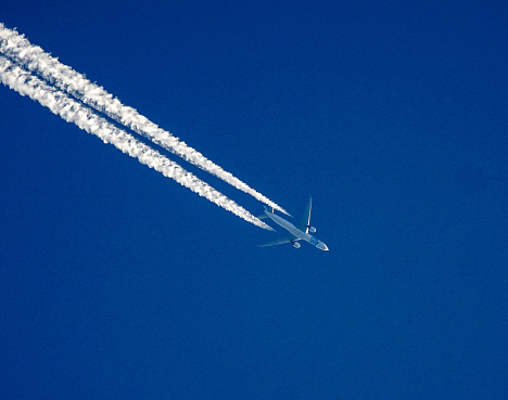 Airplane flying with high speed on blue sky background seen from the ground.