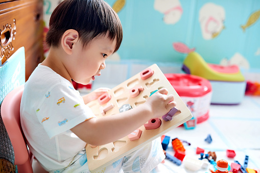 Side view of one little boy playing with numbers toy puzzle.