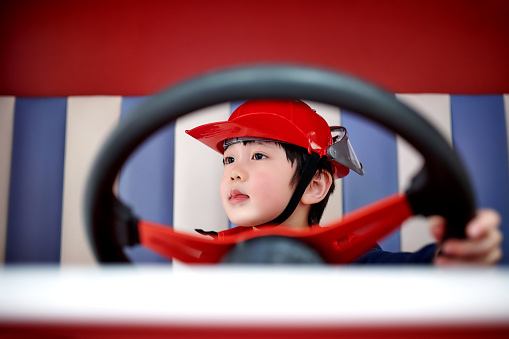 Low angle and front view of one asian little boy mitation firefighter driving fire-truck.