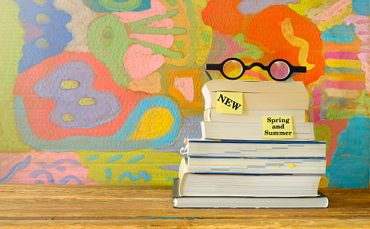 New book releases for spring 2023, with stack of books, spectacles and painted background.Spring Book fair, inspiration,reading, education, literature concept, free copy space