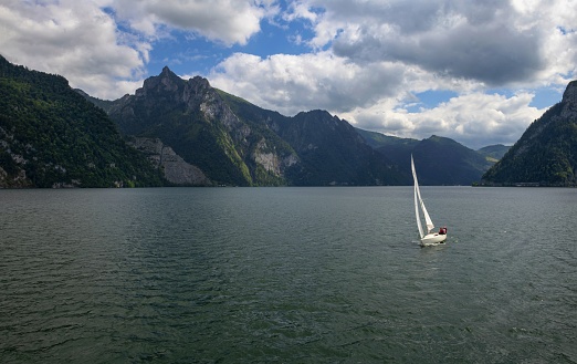 Gmunden, Austria, July 8, 2022: A sailboat floats on the Traunsee Lake in Upper Austria under cloudy summer sky. The region is also known as Salzkammergut, part of which is listed as UNESCO World Heritage Site.