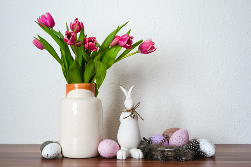 Easter eggs decorations and pussy willow twigs with catkins in a vase. Blue background, space for copy.