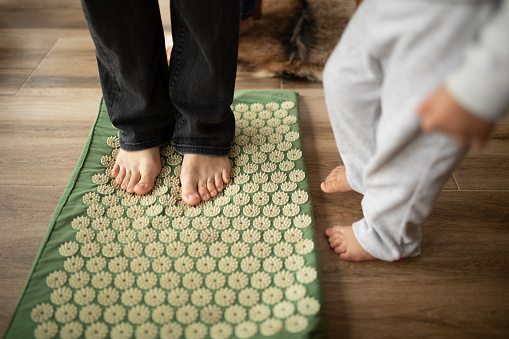 Mother enjoying her leisure time with daughter and they are exercising barefoot over mat with spikes that stimulate feet for better circulation and against flat feet .