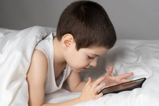 istock A 5 year old boy plays games on his phone while lying in bed. Gadgets in bed before bedtime in a child 1469773153