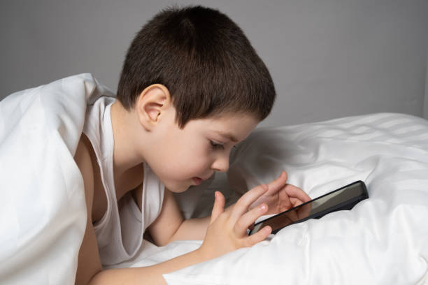istock A 5 year old boy plays games on his phone while lying in bed. Gadgets in bed before bedtime in a child 1469773164