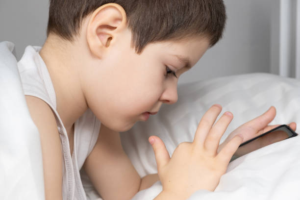 istock A 5 year old boy plays games on his phone while lying in bed. Gadgets in bed before bedtime in a child 1469773186